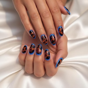 May include: A close-up of a hand with long, oval-shaped nails. The nails feature a tortoiseshell design with a black border and a bright blue outline. The nails are well-manicured and the skin is smooth.