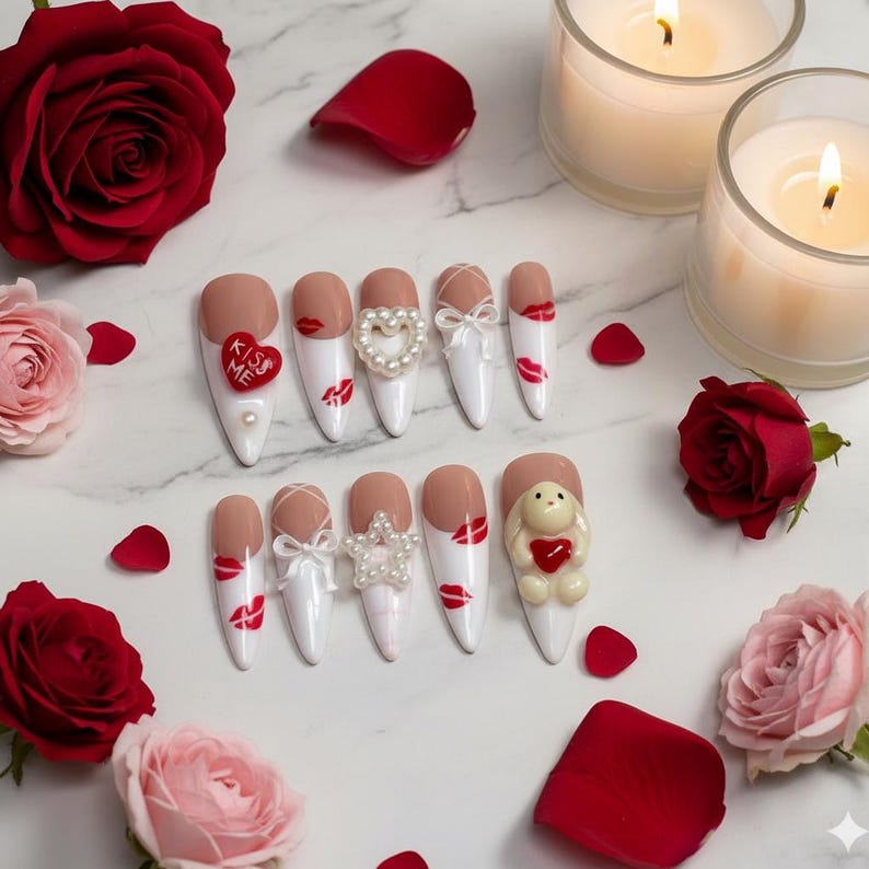 May include: A collection of artificial nails with various designs, including red lips, bows, and pearl accents. Some nails feature a "Kiss Me" heart. The arrangement is set on a marble surface, surrounded by red and pink roses, petals, and lit candles.