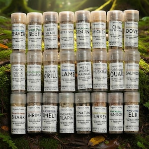 May include: A collection of twenty-four clear plastic cylindrical jars filled with dried food for hermit crabs, arranged in a grid. Each jar features a white label with the brand name OrganicCrabby, specific food ingredients, and a net weight of 4g.