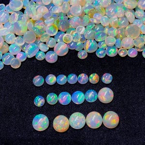 Pode incluir: Uma coleção de opalas em vários tamanhos e formas, exibindo um espectro de cores iridescentes. As opalas estão dispostas sobre uma superfície escura, realçando sua beleza natural e jogo de luzes.