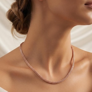 May include: A rose gold wheat chain necklace featuring a tightly woven, braided metal link design that rests against the collarbone. The necklace has a polished, metallic finish and a consistent, uniform thickness throughout the entire length of the chain.