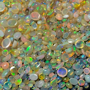 Könnte beinhalten: Nahaufnahme einer Sammlung polierter Opal-Edelsteine. Die Opale zeigen eine Vielzahl von Formen und Größen, mit Farben von Weiß über Rosa bis hin zu Grün und Blau. Die Edelsteine sind verstreut und erzeugen einen schimmernden Effekt.