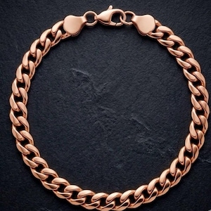 May include: A rose gold-toned curb chain bracelet featuring interlocking oval links with a polished, reflective finish. The bracelet is secured with a lobster claw clasp mechanism at the top, connecting two end caps that transition into the chain links.