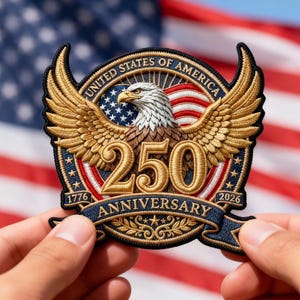May include: Embroidered patch featuring a golden eagle with outstretched wings, the text "UNITED STATES OF AMERICA", and "250 ANNIVERSARY 1776-2026". The patch is held in front of an American flag.