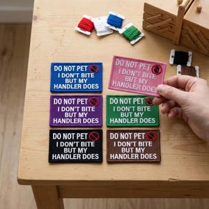 May include: Rectangular patches in various colors, including blue, pink, purple, green, black, and brown, with the text "DO NOT PET I DON'T BITE BUT MY HANDLER DOES." The patches have a red no-pet symbol. Spools of thread are also visible.