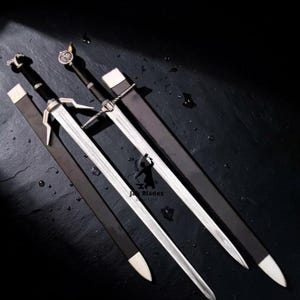 Könnte beinhalten: Zwei silberne Schwerter mit schwarzen Griffen und Scheiden werden auf einer dunklen Oberfläche gezeigt. Die Klingen sind lang und scharf, mit aufwendigen Details an den Griffen. Die Scheiden sind dunkelbraun mit weißen Spitzen. Mittelalterliches Thema.