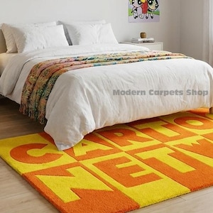 May include: A bedroom with a vibrant orange and yellow rug displaying "CARTOON NETWORK" in large letters. The rug sits before a bed with white bedding. Cartoon posters adorn the walls.