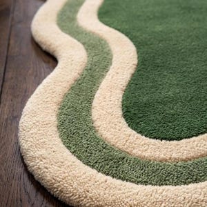May include: A green, cream, and light green wavy rug. The rug has a soft, textured surface with a cream-colored border and two wavy stripes in light green and green. The rug is placed on a dark wood floor.