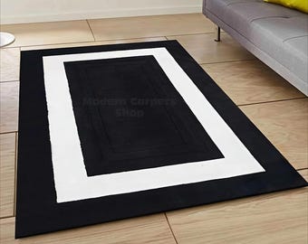 May include: A rectangular black rug with a white border and a black center. The rug is on a light brown tiled floor. The text "Modern Carpets Shop" is visible on the rug.