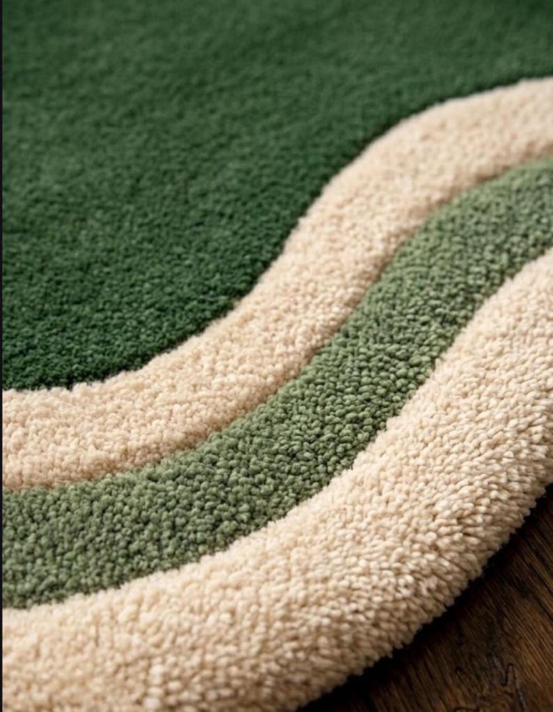 May include: Close-up of a textured rug with a wavy design. The rug features three distinct bands of color: a deep green, a lighter green, and a cream color. The rug has a soft, plush appearance.