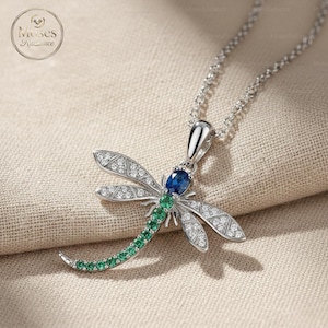 May include: A silver dragonfly pendant necklace. The dragonfly features a blue gemstone head, green gemstone tail, and clear gemstone wings. The necklace is on a silver chain.