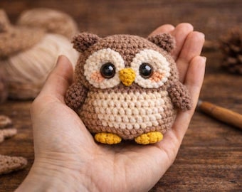 May include: A handmade crochet owl in shades of brown, cream, and yellow. The owl has large black eyes, a yellow beak, and small ear tufts. The owl is held in a hand, showcasing its size and detail. A charming, whimsical decorative item.