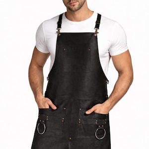 Könnte beinhalten: Schwarze Lederschürze mit verstellbaren Trägern und Metallbeschlägen. Mit zwei großen Fronttaschen mit Metallring-Akzenten und einer Brusttasche. Die Schürze ist auf Schutz und Stil ausgelegt.