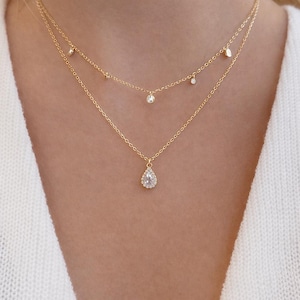 Puede incluir: Un collar dorado de varias capas con tres hilos. El hilo superior tiene pequeños adornos redondos. El hilo del medio tiene pequeñas gemas colgantes. El hilo inferior presenta un colgante en forma de lágrima con pequeñas piedras transparentes.