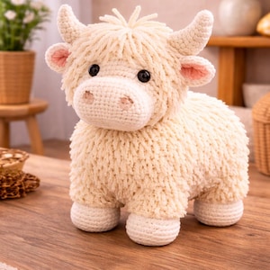 Puede incluir: Peluche de vaca de las Tierras Altas hecho a mano, de color crema. El animal de peluche tiene un cuerpo esponjoso, cuernos pequeños y el interior de las orejas rosa. Se apoya sobre cuatro patas blancas y redondeadas y tiene ojos negros.