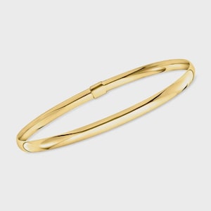May include: A gold bangle bracelet with a hinged clasp. The bracelet has a smooth, polished surface and a slightly curved design. The gold color is bright and reflective, suggesting a high-quality material.