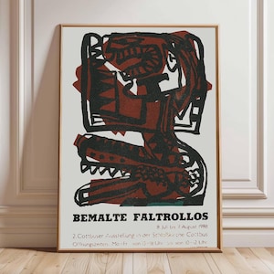 Puede incluir: Póster vintage enmarcado con un marco de madera marrón. El póster presenta un diseño abstracto audaz en negro y marrón rojizo sobre un fondo crema. El texto en la parte inferior dice "BEMALTE FALTROLLOS" y detalles sobre una exposición.