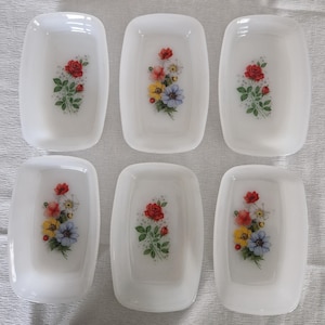 Könnte beinhalten: Sechs weiße rechteckige Schalen mit abgerundeten Ecken. Jede Schale hat ein Blumendesign mit roten Rosen, gelben, blauen und weißen Blumen. Die Schalen sind in zwei Dreierreihen angeordnet.