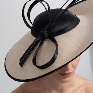 Chapéu fascinator bege com laço preto e aba larga, acessório de cabelo para ocasiões especiais, como casamentos, corridas de cavalos e festas.