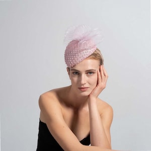 Pode incluir: Um fascinator rosa claro com um design em rede e pequenas decorações. O adorno de cabeça apresenta um detalhe delicado e transparente com babados. Este adorno de cabeça formal é adequado para ocasiões especiais.