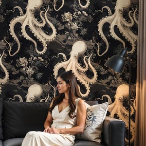 May include: Wallpaper featuring a repeating pattern of beige octopuses on a black background with floral and landscape motifs. A woman sits on a black sofa in front of the wallpaper. The wallpaper adds a unique decorative element.