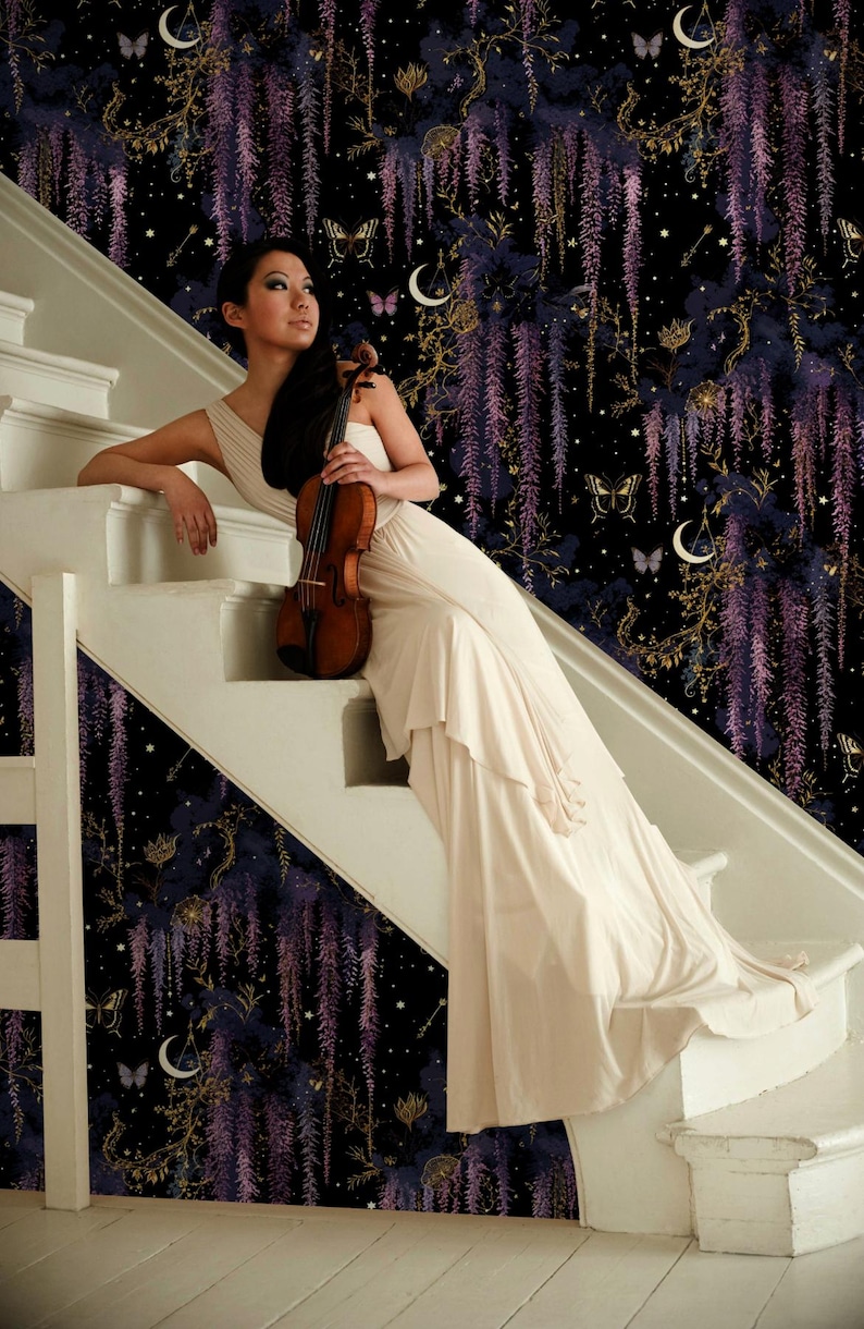 May include: A woman in a cream-colored dress sits on a white staircase, holding a violin. The background features a dark, patterned wallpaper with purple wisteria, butterflies, and celestial elements. The violin is a warm brown color.