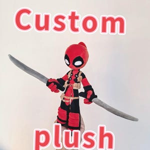 Può includere: Bambola di peluche rossa e nera di un personaggio di supereroe, con due spade grigie. La bambola ha una testa rossa con forme di occhi neri e indossa un costume rosso e nero. La parola "Custom" è sopra e "plush" sotto.