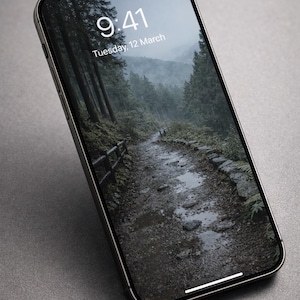 May include: A silver smartphone displays a nature scene of a path through a forest with the time 9:41 and the date Tuesday, 12 March on the screen. The phone is angled on a gray surface.