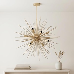 Può includere: Un lampadario dorato in stile Sputnik con più apparecchi di illuminazione. L'apparecchio ha una sfera centrale con aste radiali, creando un design a forma di stella. Il lampadario è sospeso dal soffitto.