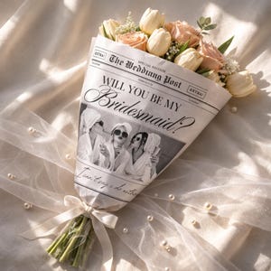 May include: A bouquet of cream and peach-colored roses and tulips wrapped in newspaper. The newspaper reads "The Wedding Post" and "Will You Be My Bridesmaid?" with a photo of women. The bouquet is tied with a cream ribbon.