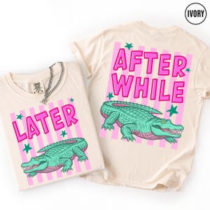 Puede incluir: Camisetas de color marfil con un dise&ntilde;o de cocodrilo de dibujos animados. Una camiseta dice "LATER" y la otra "AFTER WHILE" en letras rosas. El cocodrilo es verde con detalles rosas, sobre rayas rosas y blancas.