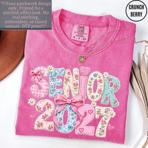 May include: A bright pink t-shirt featuring a faux patchwork graphic that reads SENIOR 2027. The letters and numbers are decorated with floral, gingham, and polka dot patterns, accented by pink bows, small hearts, and daisies. The shirt has a crew neck.