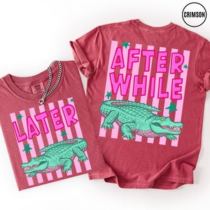 Puede incluir: Dos camisetas granates con dise&ntilde;os de rayas rosas y blancas. Una camiseta dice "LATER" y la otra "AFTER WHILE" en letras rosas. Ambas camisetas presentan un gr&aacute;fico de un caim&aacute;n verde. Las camisetas son de la marca "CRIMSON".