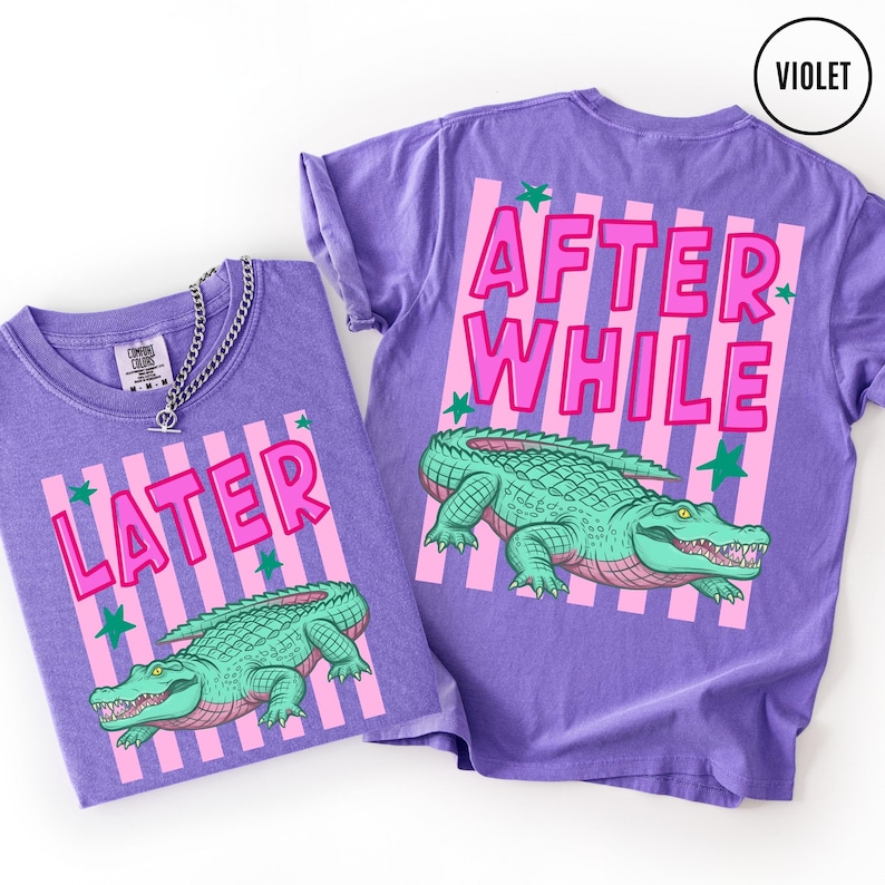 Puede incluir: Dos camisetas violetas con un dise&ntilde;o gr&aacute;fico. Una camiseta dice "LATER" y la otra "AFTER WHILE" en letras rosas. Ambas camisetas presentan una ilustraci&oacute;n de un caim&aacute;n verde con detalles rosas y rayas verticales rosas.