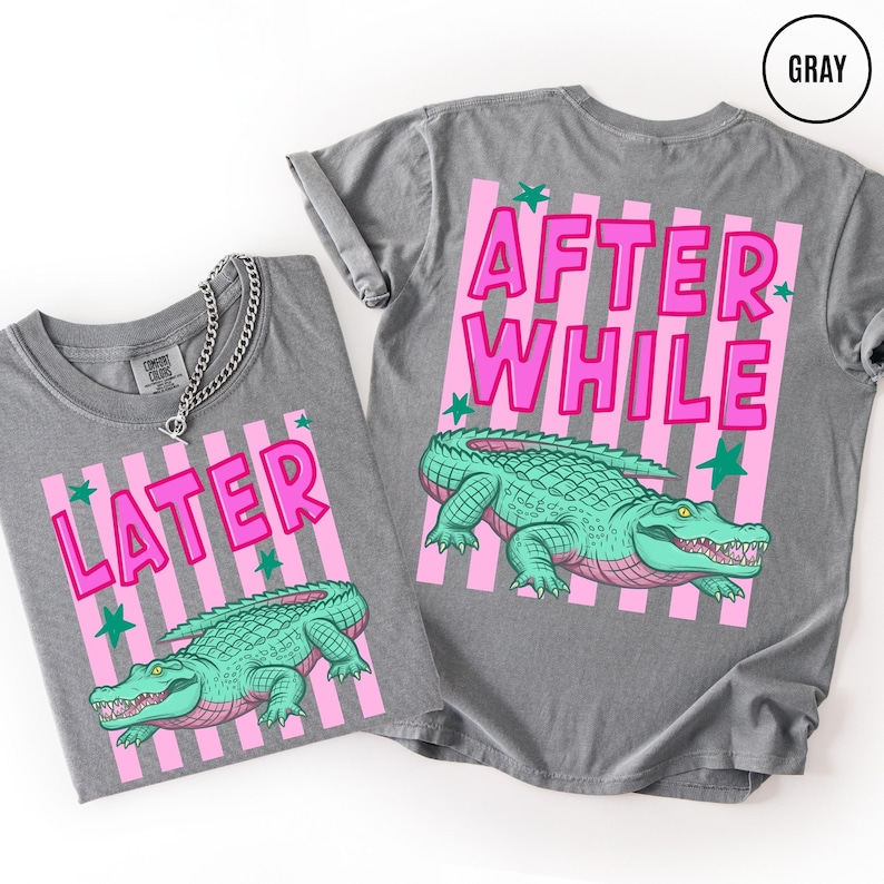 Puede incluir: Dos camisetas grises con dise&ntilde;os de rayas rosas y blancas. Una camiseta dice "LATER" y la otra "AFTER WHILE" en letras rosas. Ambas camisetas presentan una ilustraci&oacute;n de un caim&aacute;n verde.