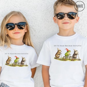 May include: Two white t-shirts featuring a graphic of a hamster, a frog, and a hedgehog wearing party hats. The hamster and hedgehog ride scooters, while the frog rides a bicycle. The text reads, Off To Cause Maximum Kerfuffle.