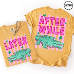 Puede incluir: Camisetas de color mostaza con las frases "LATER" y "AFTER WHILE" en letras rosas. Cada camiseta presenta un gr&aacute;fico de un caim&aacute;n verde. Rayas verticales rosas y estrellas verdes acent&uacute;an el texto y el caim&aacute;n.