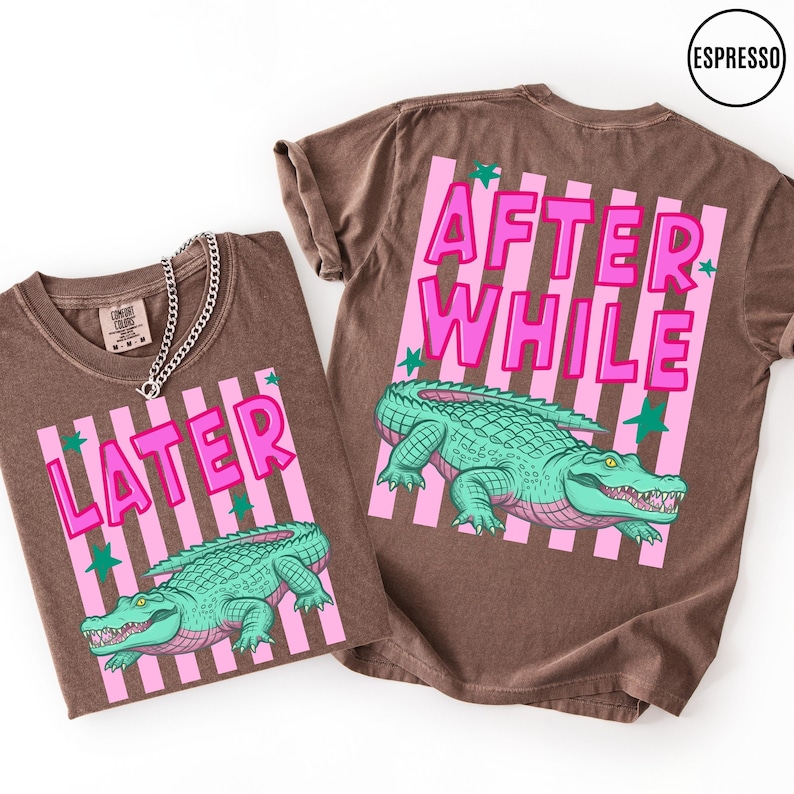 Puede incluir: Dos camisetas marrones con los textos "LATER" y "AFTER WHILE" en rosa, con un gr&aacute;fico de un cocodrilo verde. Las camisetas tienen un fondo a rayas rosas y detalles de estrellas verdes. Una camiseta tiene un collar de cadena plateada.