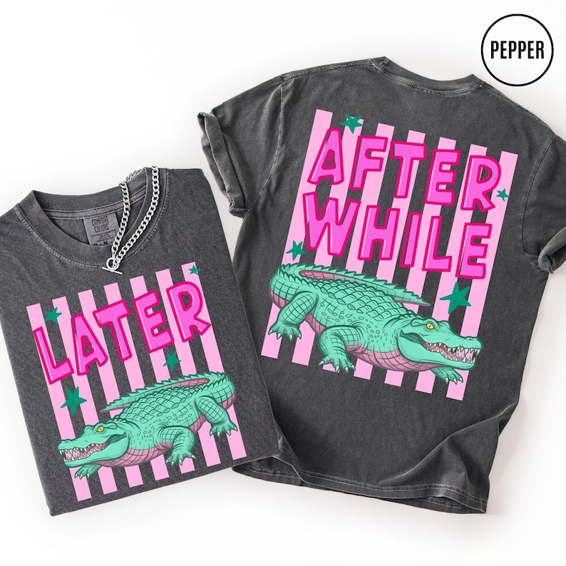 Puede incluir: Dos camisetas gris oscuro con un dise&ntilde;o de rayas rosas y blancas. Una camiseta dice "LATER" y la otra "AFTER WHILE" en letras rosas. Ambas camisetas presentan una ilustraci&oacute;n de un caim&aacute;n verde.