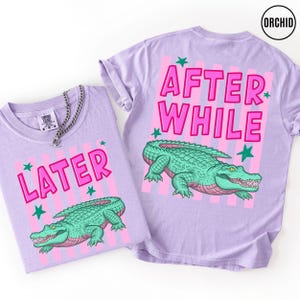 Puede incluir: Dos camisetas lavanda con dise&ntilde;os a juego. Una muestra "LATER" en rosa con un caim&aacute;n verde. La otra tiene "AFTER WHILE" en la espalda, tambi&eacute;n con un dise&ntilde;o de caim&aacute;n. Rayas rosas y estrellas verdes completan el dise&ntilde;o.