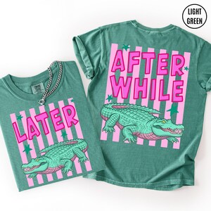 Puede incluir: Dos camisetas verde claro con dise&ntilde;os de rayas rosas y las palabras "LATER" y "AFTER WHILE" en letras rosas. Cada camiseta presenta una ilustraci&oacute;n de un caim&aacute;n verde con acentos rosas. Las camisetas son ropa casual.