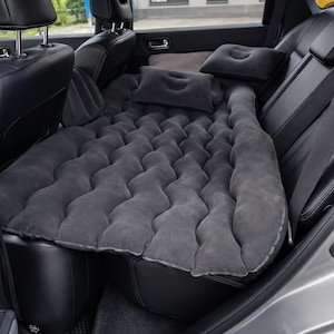 Puede incluir: Una cama inflable gris instalada en el asiento trasero de un vehículo. El juego incluye un colchón y dos almohadas. Los asientos del coche son de cuero negro. La cama para coche está diseñada para la comodidad durante el viaje. El colchón mide unos 150 cm.