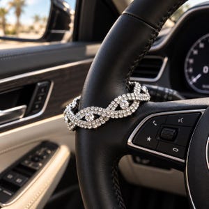 Puede incluir: Una pulsera de tono plateado con un patrón entrecruzado de pedrería transparente y brillante. El accesorio está envuelto alrededor del borde de cuero negro de un volante de coche, mostrando un diseño flexible con varias filas de cristales.
