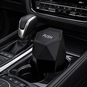 May include: A black, geometric-shaped car trash can with the word "PUSH" printed on the top. The trash can is placed in a car's cup holder, next to the gear shift.