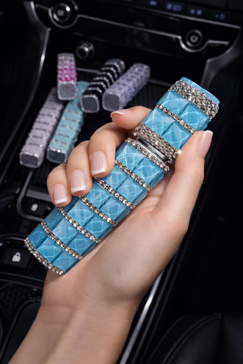 Puede incluir: Un ambientador rectangular azul claro para coche con un patr&oacute;n de diamantes y detalles de pedrer&iacute;a. Varios ambientadores de otros colores son visibles en el fondo.