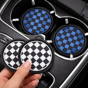 May include: Set of car coasters with a checkered pattern in black and white, and blue and black. The coasters are round and made of a rubbery material. The coasters are shown in a car's cup holders.