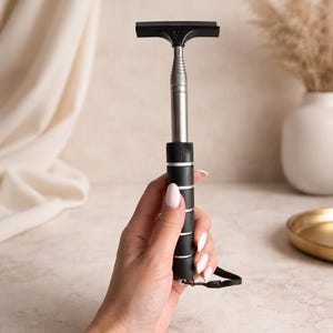 Könnte beinhalten: Ein schwarzer und silberner Fensterabzieher mit Teleskopstiel. Der Abzieher hat eine schwarze Gummilippe und einen schwarz-silbernen Griff. Der Griff hat eine schwarze Handschlaufe. Das Produkt ist zum Reinigen von Fenstern bestimmt.