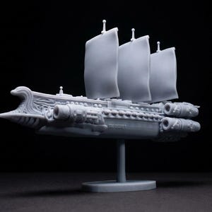 May include: A grey model ship with three sails, displayed on a stand against a black backdrop. The ship features detailed hull elements and is a miniature representation of a sailing vessel.