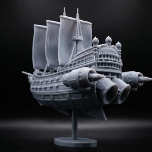 May include: A grey model of a sailing ship with jet engines attached. The ship has three sails and multiple jet engines. It is mounted on a grey stand against a black background.