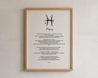 May include: A framed print featuring the Pisces zodiac symbol and a poetic description of the sign's characteristics. The text is in black on a cream-colored background, framed in light wood. The print is a decorative item.